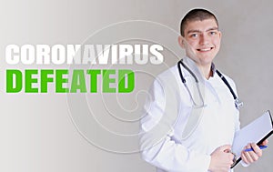 Young caucasian doctor rejoicing because of defeated coronavirus and standing in grey wall background.