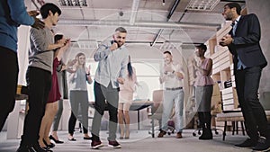 Young Caucasian employee dancing with colleagues, celebrating business achievement at casual office party slow motion.