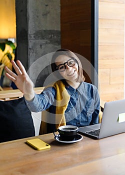 a young Caucasian, European woman in a blue denim shirt and glasses is working on a laptop