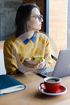a young Caucasian, European woman in a blue denim shirt and glasses is working on a laptop