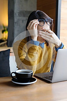 a young Caucasian, European woman in a blue denim shirt and glasses is working on a laptop