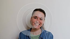 Young Caucasian European woman laughs and little embarrassed on white background. Girl in green Tshirt and denim shirt is emotiona