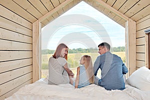 Young Caucasian family couple with baby daughter in a small modern rustic house with a large window. Lying on the bed