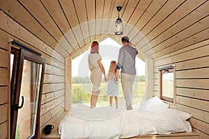 Young Caucasian family couple with baby daughter in a small modern rustic house with a large window. Lying on the bed