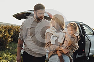 Young Caucasian Family Enjoying Road Trip, Mother and Father with Little Daughter Outdoors with SUV Car on the