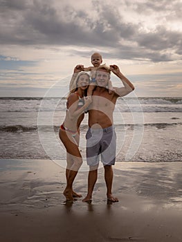 Young Caucasian family of father, mother and son spending time on the beach. Father carrying child on neck. Summer vacation