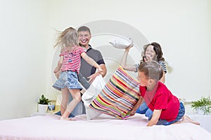 Young Caucasian Family of Four Having a Playful Funny Pillow Fight on Bed Indoors.
