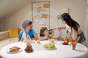 Young caucasian family, mother and her two cute little kids smiling and communicating while sitting at the kitchen table