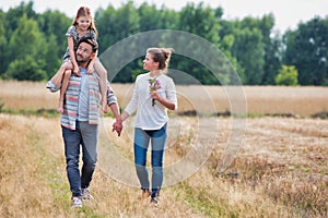 Young Caucasian family walking across field with young girl holding bouquet of flowers, concept organic ecologically friendly fami photo