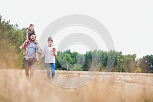 Young Caucasian family walking across field with young child on her fathers shoulders with the wife holding a bouquet of flowers