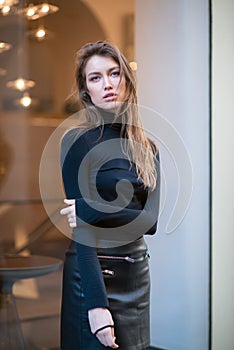 Young caucasian fashionable woman dressed in black clothes posing outdoor over Christmas Eve lights. Beautiful caucasian girl in