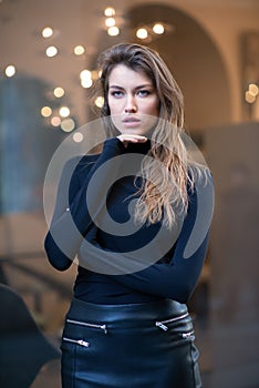 Young caucasian fashionable woman dressed in black clothes posing outdoor over Christmas Eve lights. Beautiful caucasian girl in