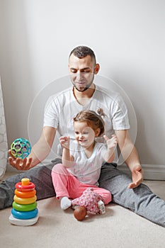 Young Caucasian father playing with child girl. Male man parent entertains toddler daughter sitting at home.