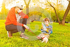 Young caucasian father and son in medical protective masks stay in park at sunny day on grass. Dad and child walk