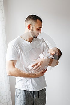 Young Caucasian father trying to calm down newborn baby. Male man parent holding rocking child daughter son on his hands.