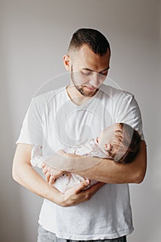 Young Caucasian father trying to calm down newborn baby. Male man parent holding rocking child daughter son on his hands.