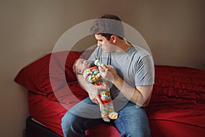 Young Caucasian father trying to calm down newborn baby. Male man parent holding rocking child on his hands