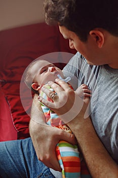 Young Caucasian father trying to calm down newborn baby. Male man parent holding rocking child on his hands