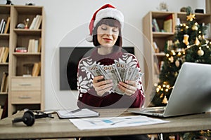 Young caucasian female accountant in Santa hat holding cash banknotes