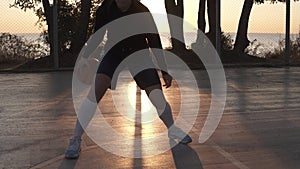 Young caucasian female basketball player dribbling and practicing ball handling skill on court. Morning dusk, sun shines