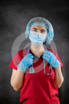 young caucasian female doctor nurse in red uniform, mask and rubber gloves with stethoscope