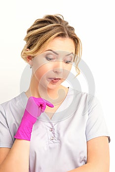 Young caucasian female doctor wearing gloves thoughtful looking down against a white background.