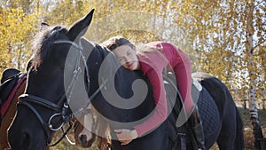 Young Caucasian female equestrian lying on horseback and caressing her pet. Graceful black horse standing in the autumn