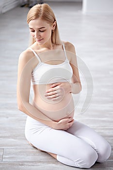 young caucasian female gravid or expectant sit on floor in studio relaxing having rest