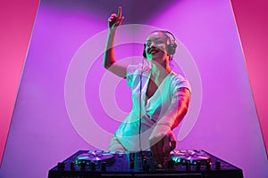 Young caucasian female musician in headphones performing on purple background in neon light