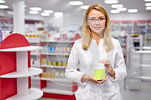 Young caucasian female pharmacist is showing medicine box presentation in pharmacy store