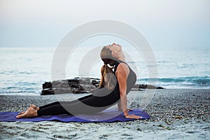 Young caucasian female practicing yoga on the seaside