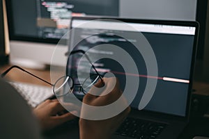 Young caucasian female programmer in glasses writes program code on a laptop