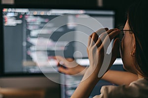 Young caucasian female programmer in glasses writes program code on a laptop