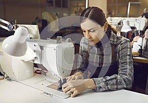 Young caucasian female shoemaker working sewing on machine at workplace