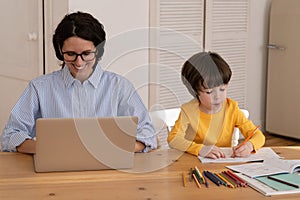 Young caucasian female work on laptop as son draws. Remote home office at covid-19 lockdown concept