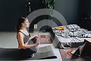 Young caucasian fitness woman meditate, doing yoga indoors at home near the bed. Staying fit and healthy