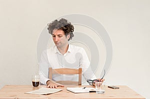 Young, Caucasian freelancer man sitting in his home office at the table in front of empty clear wall.