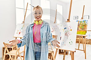 Young caucasian girl at art studio smiling cheerful with open arms as friendly welcome, positive and confident greetings
