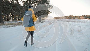 A young caucasian girl with backpack going on winter forest road in snow covered winter pine forest at sunset. Walk