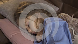 Young caucasian girl in blue sweater taking temperature. Close-up of a little sick brunette child laying under the warm