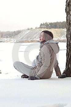 A young Caucasian girl in a brown coat staring into the distance on the horizon line between the sky and the frozen lake in winter