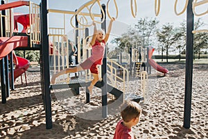 Young Caucasian girl hanging on monkey bars in park on a playground. Summer outdoor activity for kids. Active preschool child