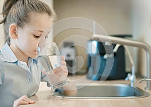 Young caucasian girl is holding a glass with water. Concept of good quality clean water. Kitchen faucet. Pouring fresh drink.