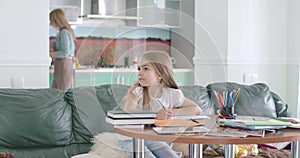 Young Caucasian girl with long hair and brown eyes doing homework at home. Cute child turning back and looking at mom