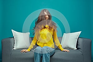 Young caucasian girl with long hairs shaking head, having fun, enjoying hair after haircare treatment, sitting on sofa