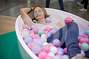 Young caucasian girl is lying in the bath with multi-colored plastic balls and smiling with closed eyes. close-up, soft