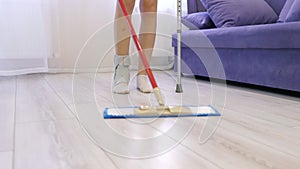 A young Caucasian girl moves around the house on one crutch and cleans the floors with a mop with one hand. Leg injury