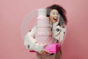 Young caucasian girl with open mouth looks at camera in surprise, holds boxes on pink background.