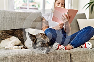 Young caucasian girl smiling happy sitting on the sofa with dog reading book at home