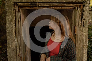Young Caucasian girl standing in front of an old wooden door of an abandoned house